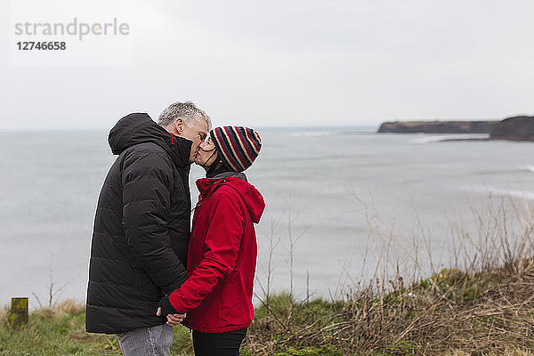 Zärtliches Paar  das sich auf einer Klippe mit Blick auf das Meer küsst