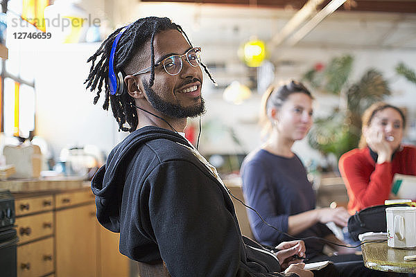 Porträt lächelnder junger Mann mit Kopfhörern am Küchentisch