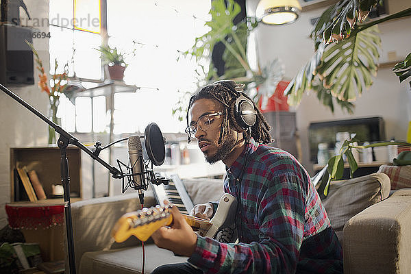 Junger männlicher Musiker  der in einer Wohnung Musik aufnimmt und am Mikrofon Gitarre spielt