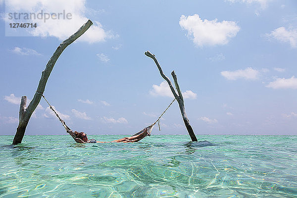 Frau liegt in Hängematte über dem ruhigen Ozean  Malediven  Indischer Ozean