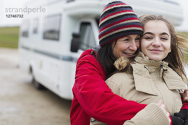 Zärtliche Mutter und Tochter in warmer Kleidung umarmen sich vor dem Wohnmobil