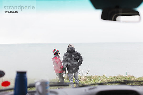 Ein Paar steht vor einem Wohnmobil auf einer Klippe mit Blick auf den Ozean