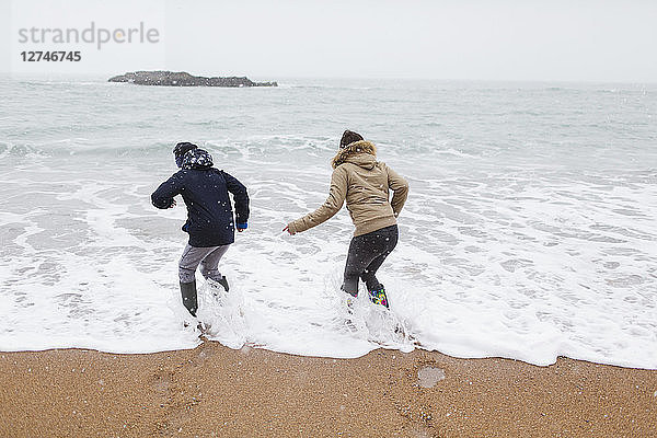 Verspielter Teenager-Bruder und Tochter spielen in der winterlichen Meeresbrandung