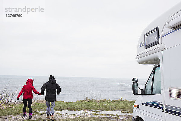 Paar hält sich vor einem Wohnmobil mit Blick auf das Meer an den Händen