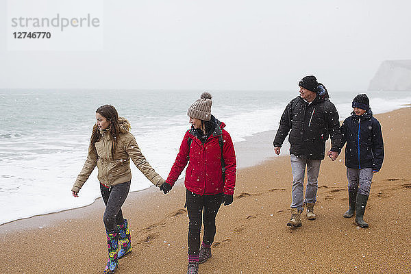 Familie in warmer Kleidung bei einem Spaziergang am verschneiten Winterstrand