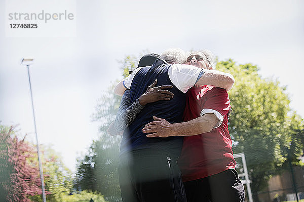 Active senior men friends hugging in sunny park