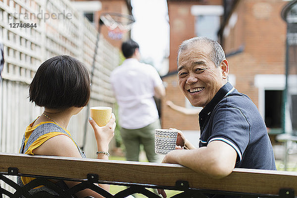 Portrait happy senior man drinking tea with family in back yard