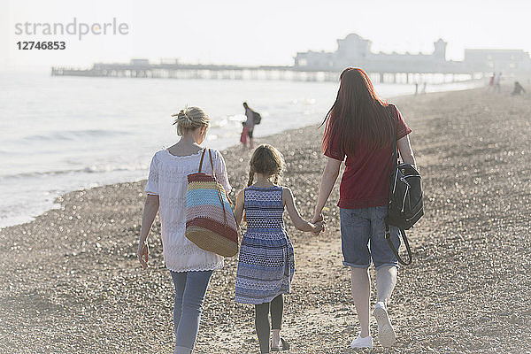 Lesbian couple and daughter walking on sunny beach