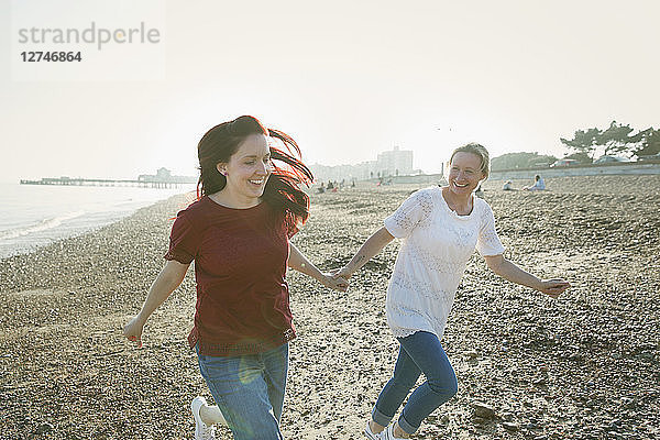 Playful  affectionate lesbian couple holding hands and running on sunny beach