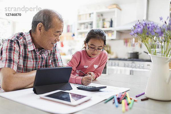 Grandfather and granddaughter coloring and using digital tablet in kitchen