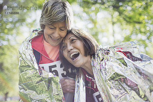 Happy active senior women friends hugging after sports race  wrapped in thermal blanket