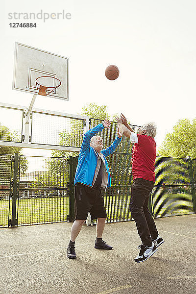 Active senior men friends playing basketball in park