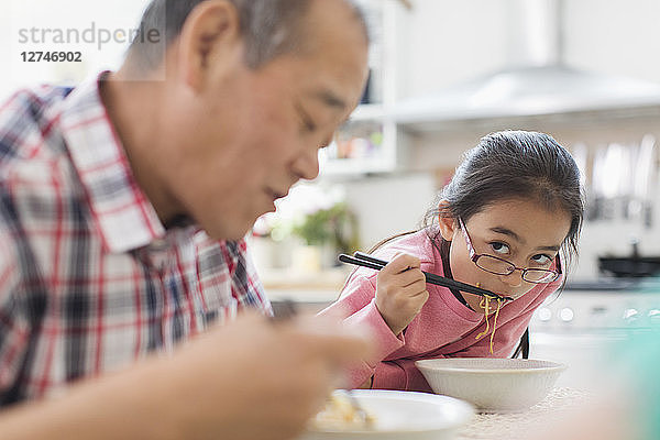Grandfather and granddaughter eating noodles in kitchen