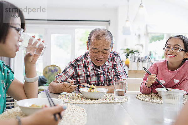 Multi-generation family eating noodles with chopsticks at table