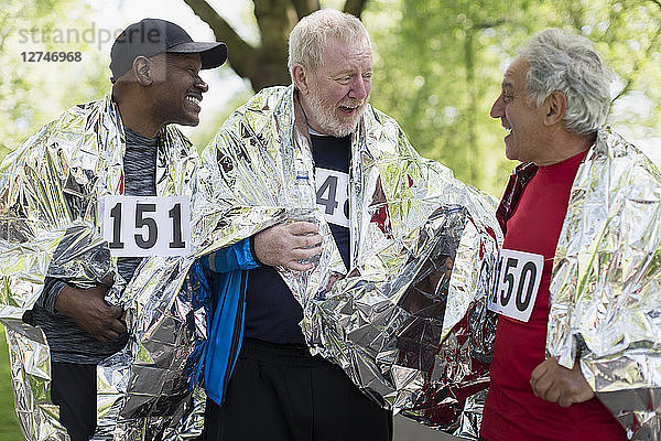 Active senior men friends finishing sports race  wrapped in thermal blankets