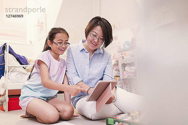 Mother and daughter using digital tablet on bedroom floor