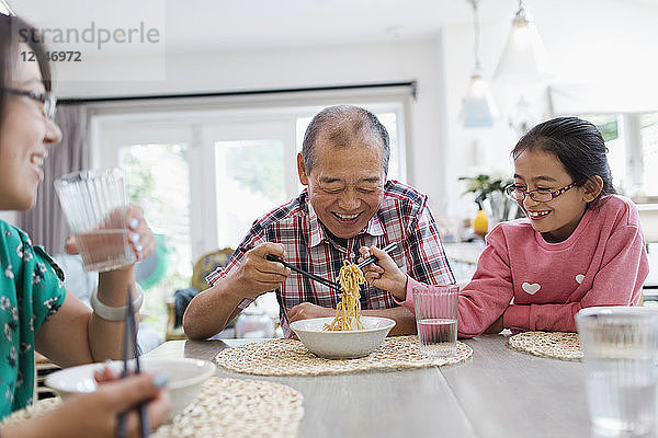 Grandfather and granddaughter sharing noodles at table