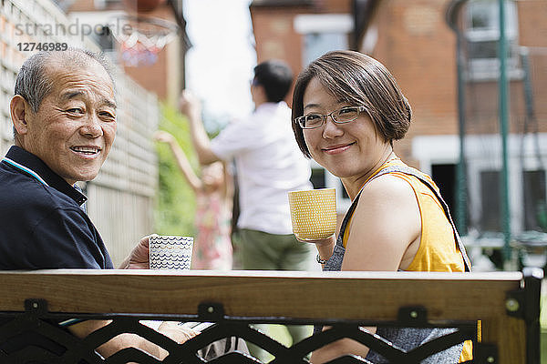 Portrait smiling daughter and senior father drinking tea on bench in yard