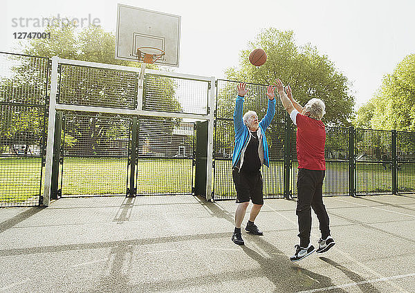 Active senior men friends playing basketball in sunny park