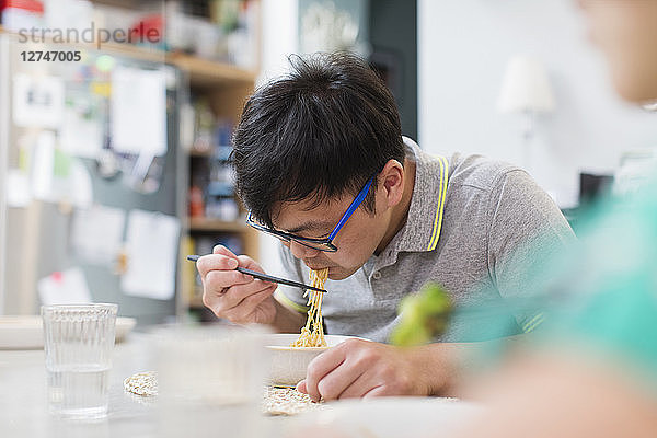 Man eating noodles with chopsticks at table