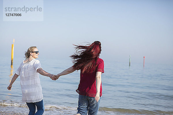 Affectionate lesbian couple holding hands on sunny ocean beach