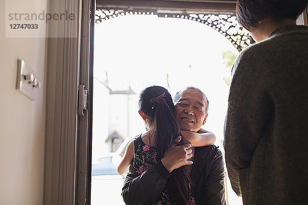 Affectionate granddaughter greeting and hugging grandfather in doorway