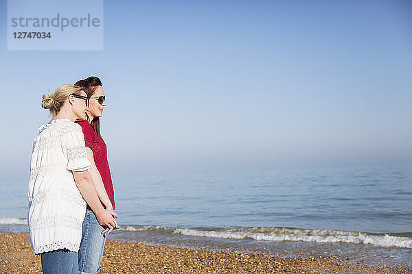 Affectionate lesbian couple holding hands on sunny ocean beach