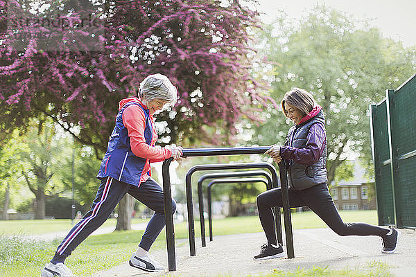 Active senior female runners stretching legs in park