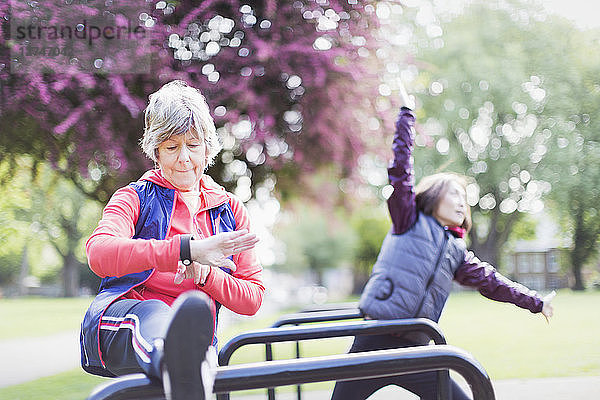 Active senior female runner stretching leg and checking smart watch