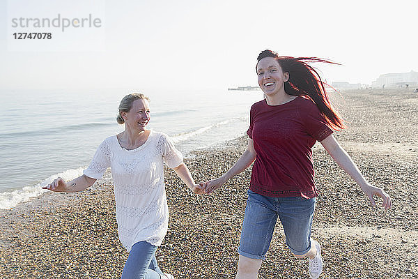 Playful lesbian couple running on sunny beach