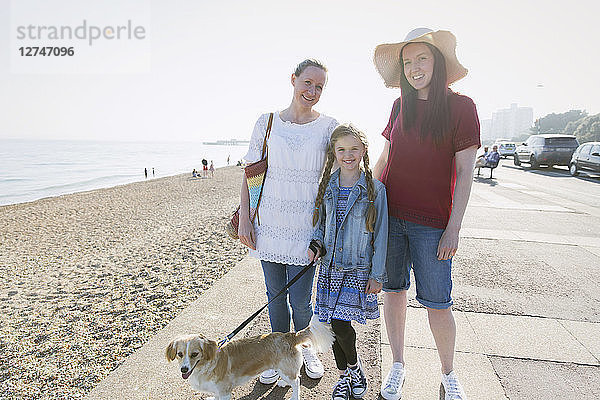 Portrait smiling lesbian couple with daughter and dog on sunny beach boardwalk
