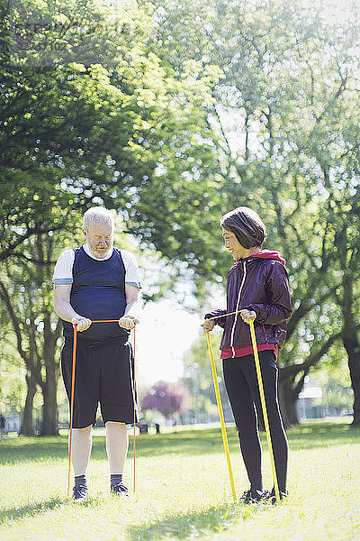 Active senior couple exercising  stretching with resistance bands in sunny park