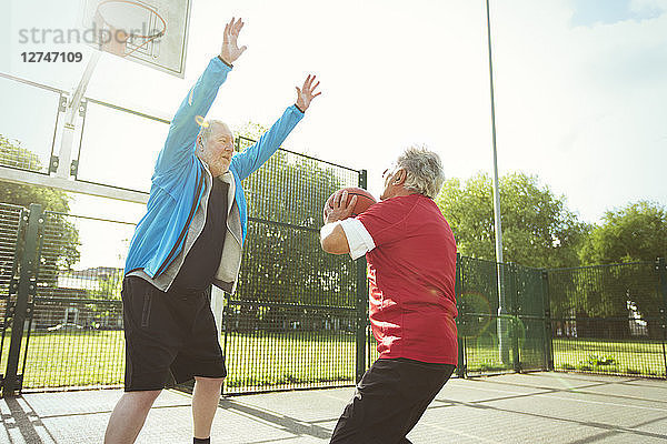 Active senior men playing basketball in sunny park