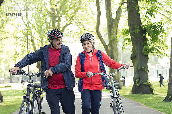 Active senior couple walking bikes in park