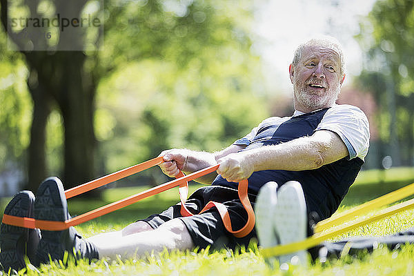 Active senior man exercising in park  stretching with resistance band