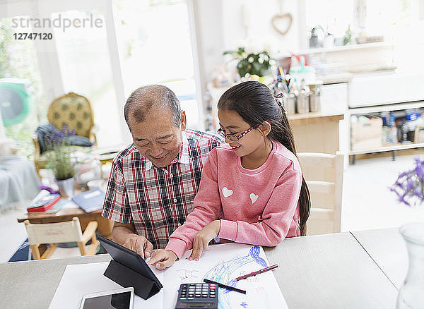 Grandfather and granddaughter using digital tablet at table