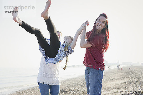 Playful lesbian couple swinging daughter on beach