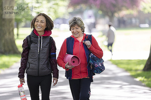 Active senior women friends with yoga mat walking in park