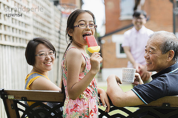 Portrait happy girl eating flavored ice with multi-generation family in back yard
