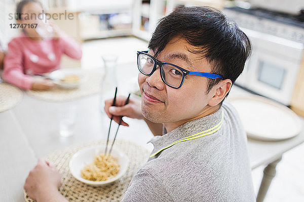 Portrait smiling man eating noodles with chopsticks at table