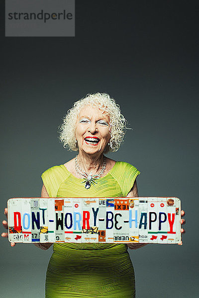 Portrait happy senior woman holding Dont Worry Be Happy license plates
