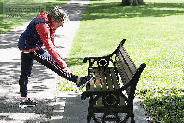 Active senior woman stretching leg on park bench