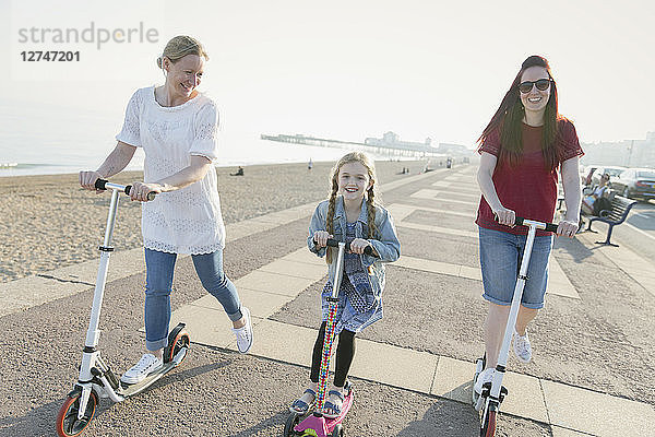 Lesbian couple and daughter riding push scooters on sunny beach