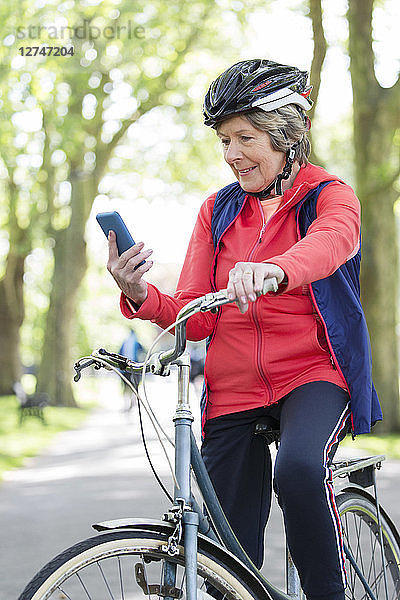 Active senior woman using smart phone on bike in park