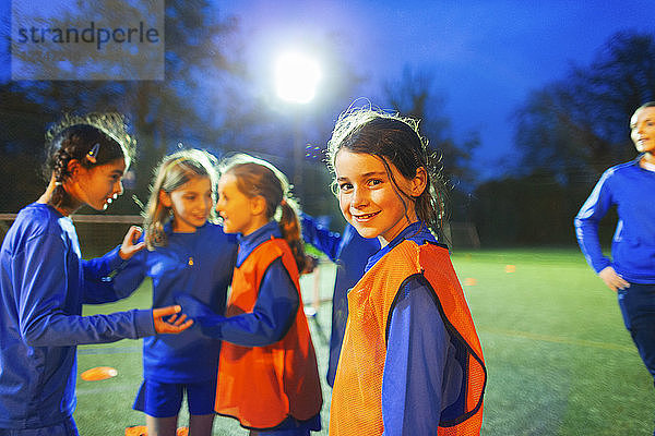 Porträt einer selbstbewussten Fußballspielerin auf dem Feld mit ihrer Mannschaft bei Nacht