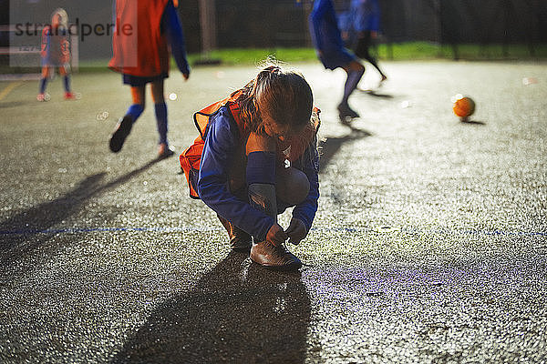 Mädchenfußballspieler bindet nachts auf dem Feld den Schuh