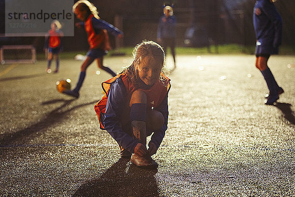 Portrait lächelnd Mädchen Fußballspieler binden Schuh auf dem Feld in der Nacht
