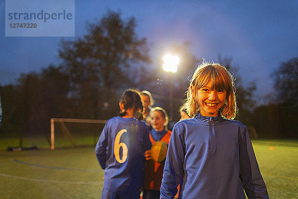 Porträt selbstbewusstes Mädchen spielt Fußball mit Team auf Feld bei Nacht