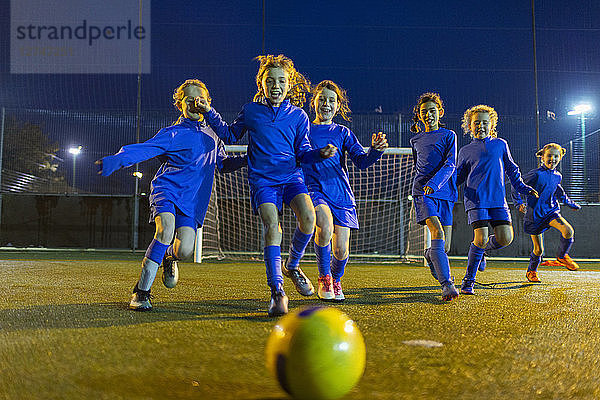 Spielende Mädchenfußballmannschaft  die nachts auf dem Feld zum Ball läuft