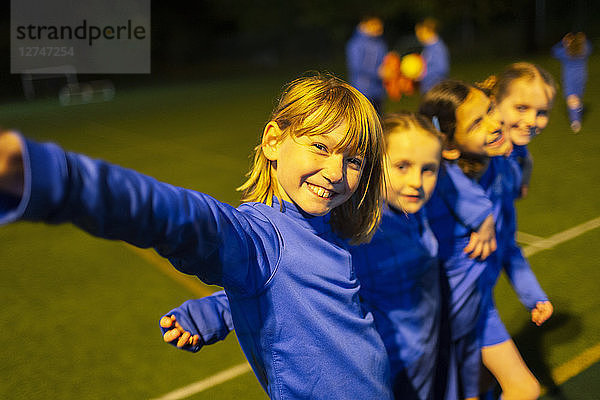 Porträt einer lächelnden  selbstbewussten Mädchenfußballmannschaft auf dem nächtlichen Spielfeld